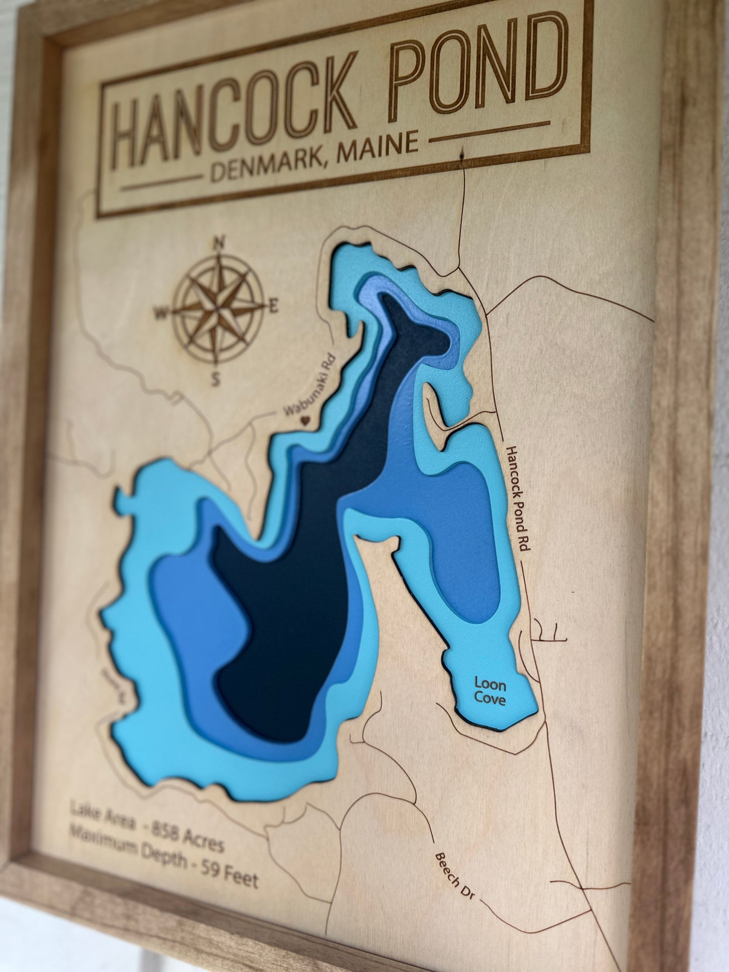 Wooden map of Hancock Pond, Denmark, Maine with blue water and brown land.