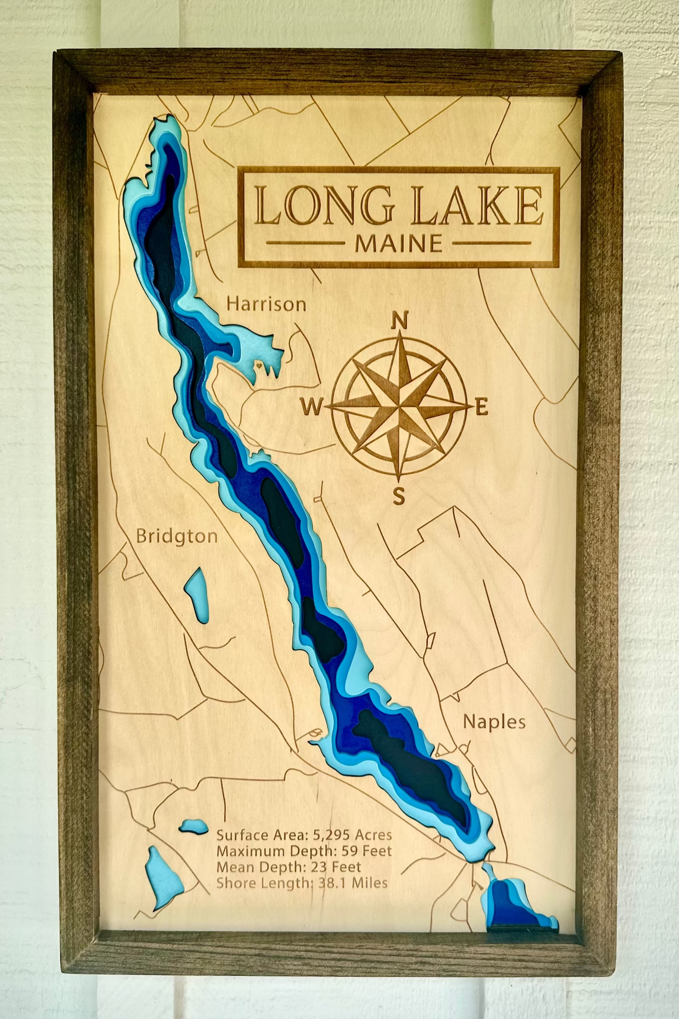 Wooden map of Long Lake, Maine with a compass and water depth indicators.